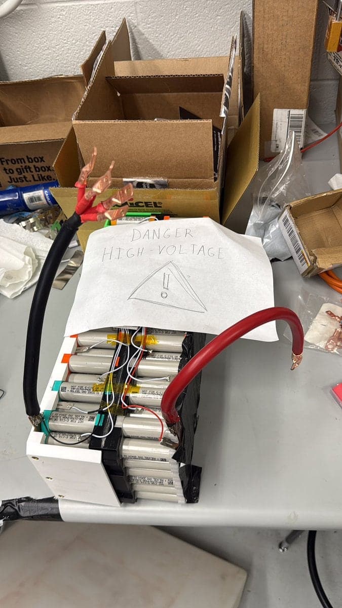 The battery pack on a bench mid-build, with thick red and black cables and a hand-drawn danger high-voltage sign on top